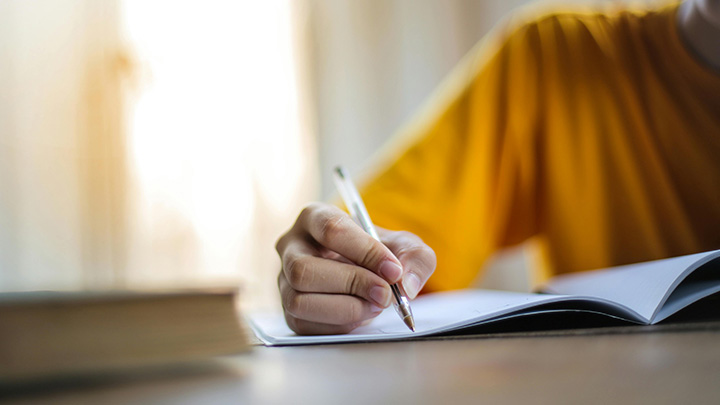 Close up of hand holding a pen, writing in a workbook