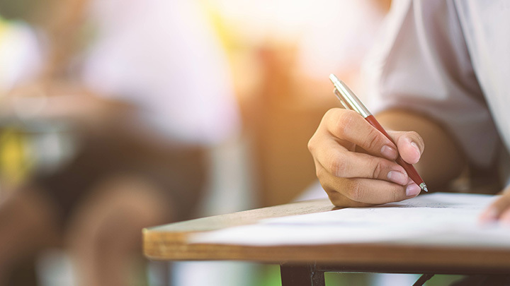 Hand holding a pen, writing on a small desk