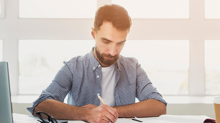 Man at desk, writing on a notepad