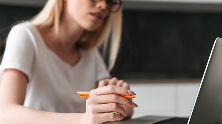 Woman working at laptop holding orange pen